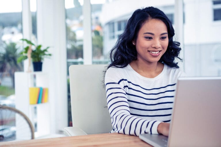 Smiling Asian woman using laptop in office