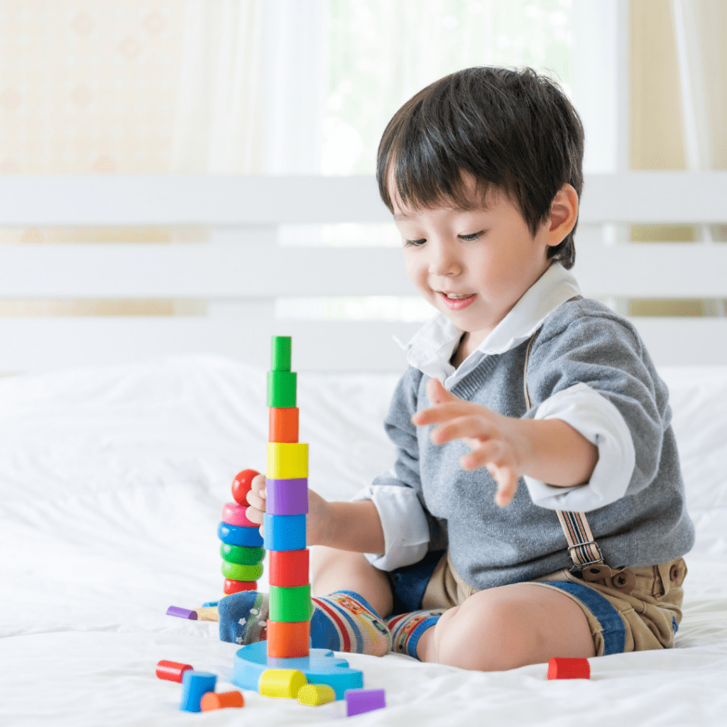 Asian cute boy sitting on bed and joyful with colorful wooden learning toy in the bedroom, copy space