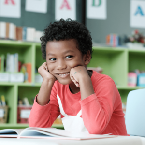 Little cute handsome black little boy sits reading in his classroom while sitting at his school desk