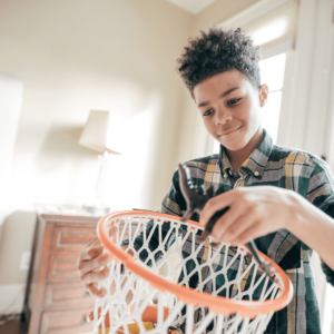 Young black boy plays with a toy dinosaur and a basketball hoop.