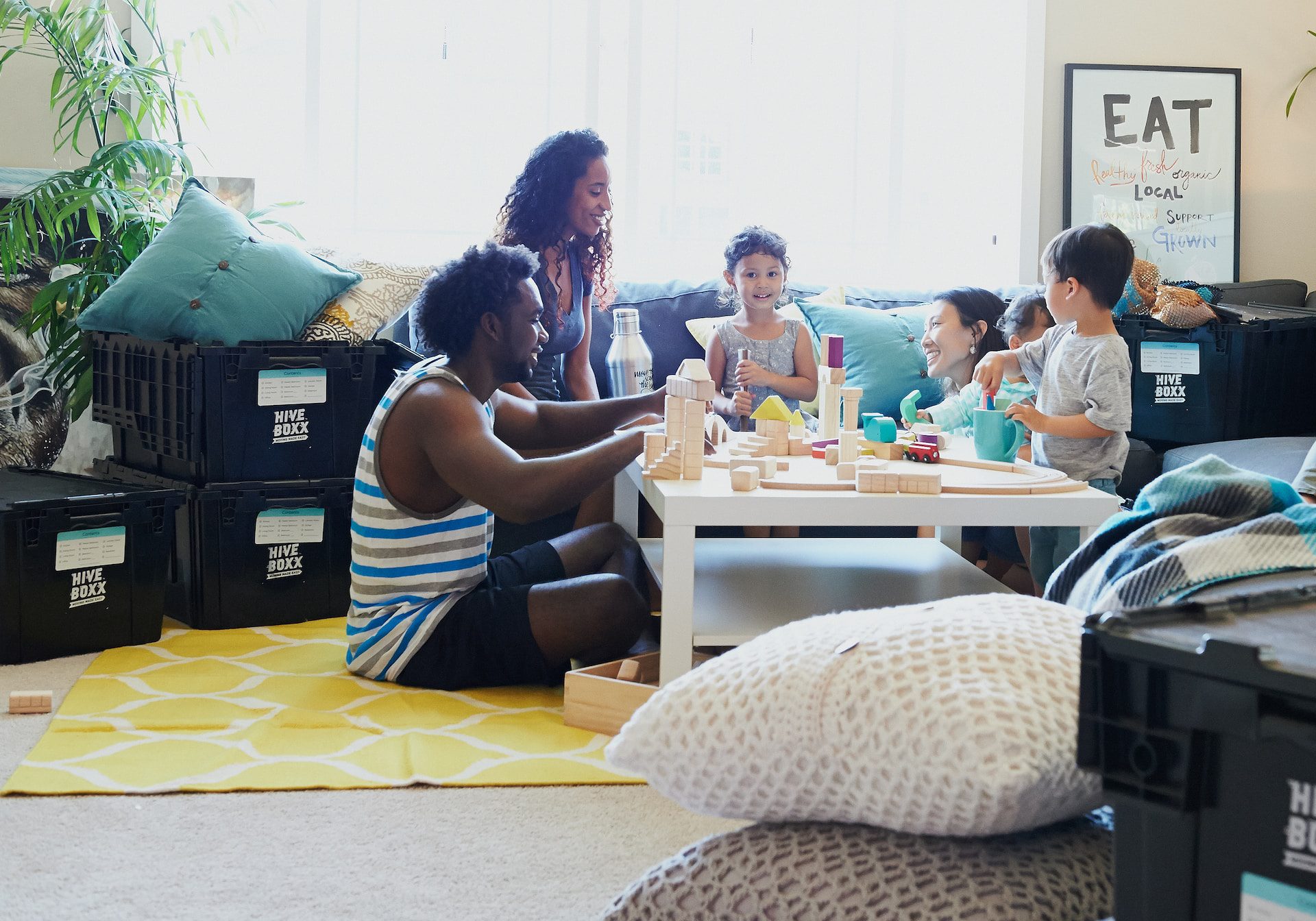 Boys and girls and moms and dads play with wooden blocks on a coffee table in their home together.