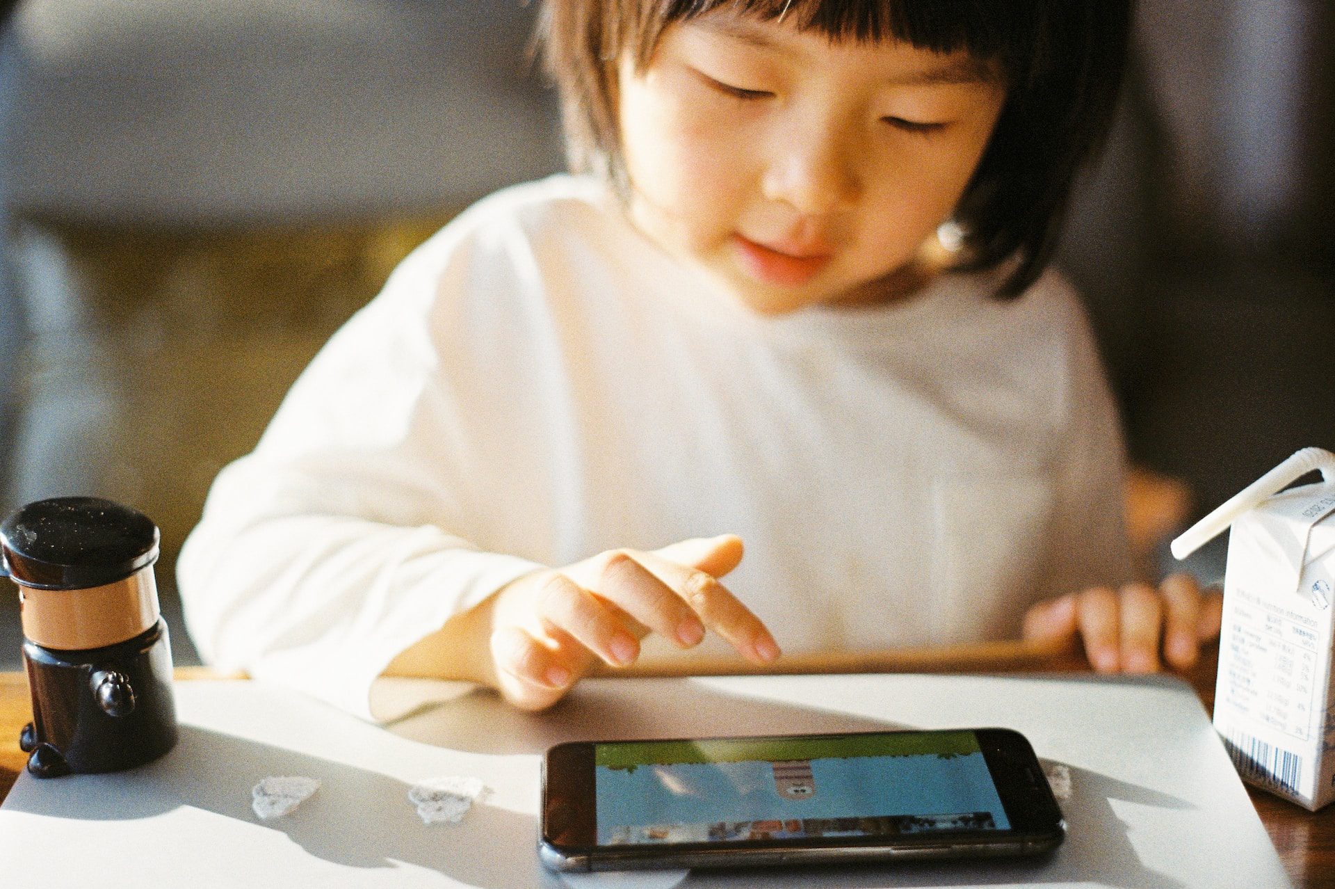 Young Asian child drinks form a juice box and plays a game on a tablet.