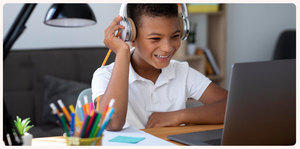 Little African American boy smiles as he receives his online virtual speech pathology speech therapy session with his speech therapist from Connect Teletherapy via a laptop.