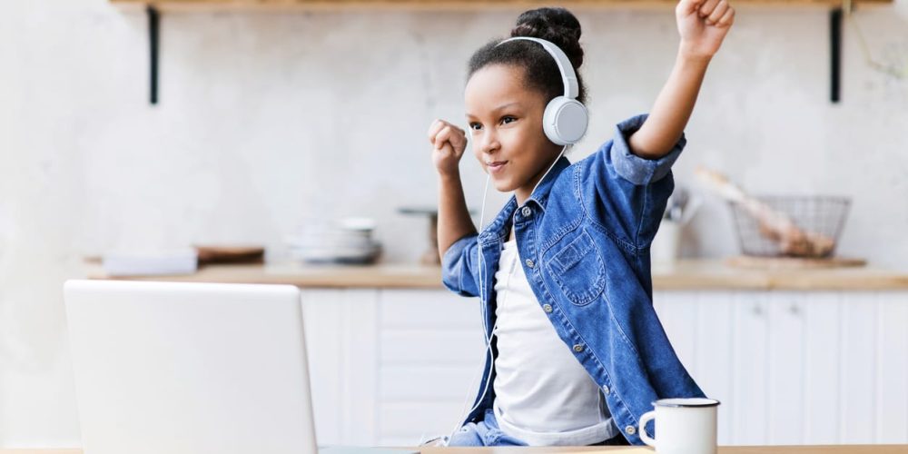 Cute little girl with laptop and headphones listening to music and dancing while studying
